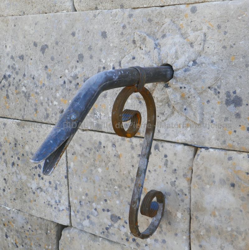 Sortie d'eau en fer forgé et rosace sculptée en pierre sur le fronton de notre fontaine de jardin