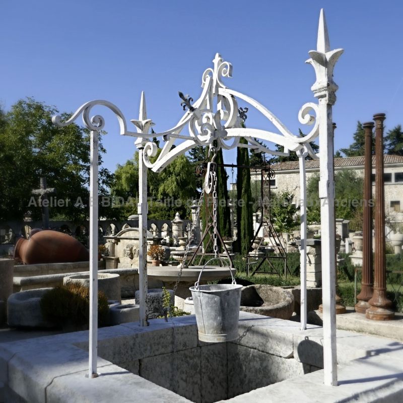 Photo of the wrought iron well-top fixed on the stone well on sale at Atelier Alain BIDAL.