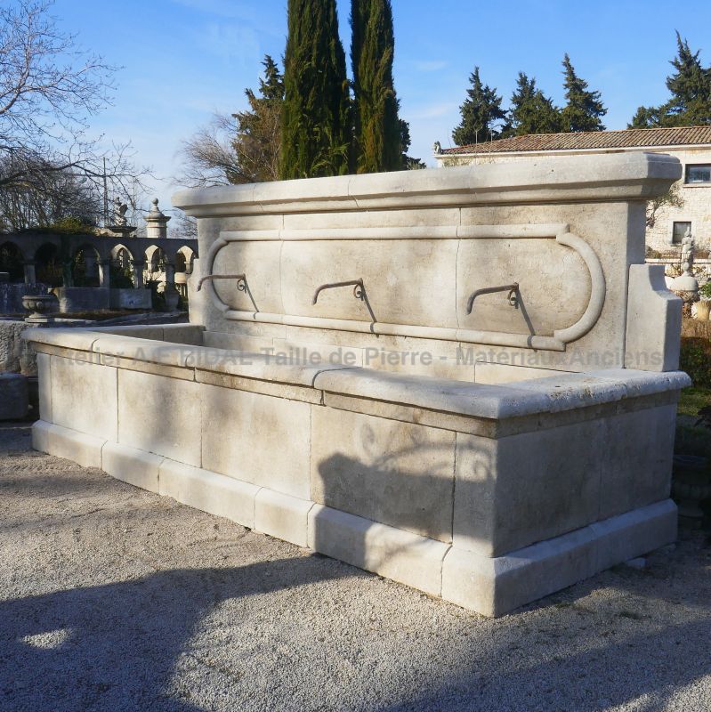 Large outdoor wall fountain in stone with deep basin and carved pediment decorated with three water outlets in wrought iron