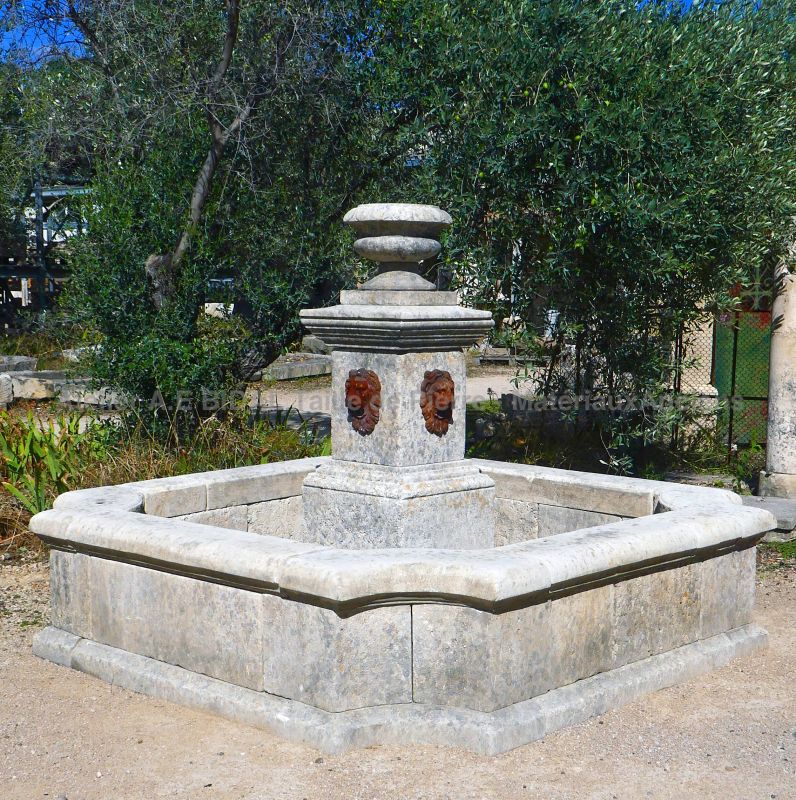 Colonne centrale en pierres vieillies avec sorties d'eau têtes de lion en fonte et vase godronné en pierre