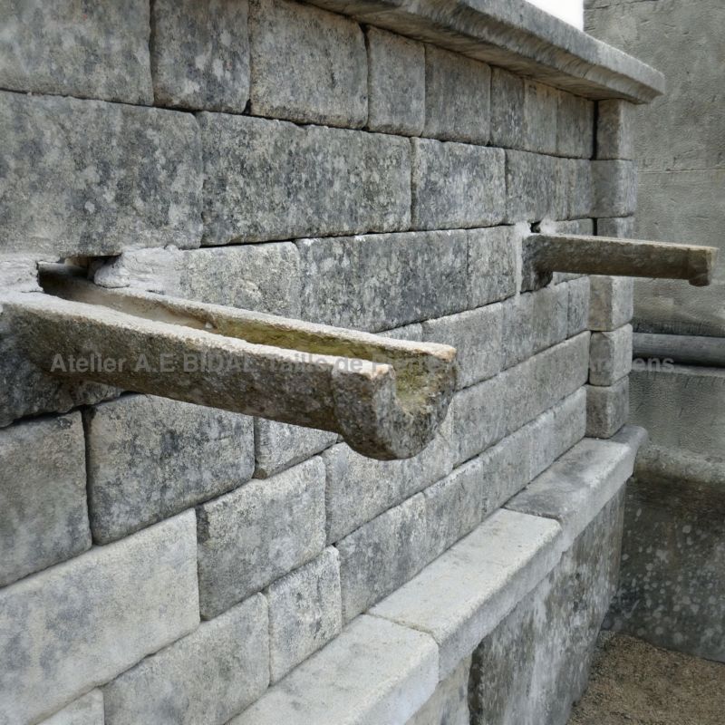 Detail of large carved gargoyles in stone on the pediment of our large rustic wall fountain.